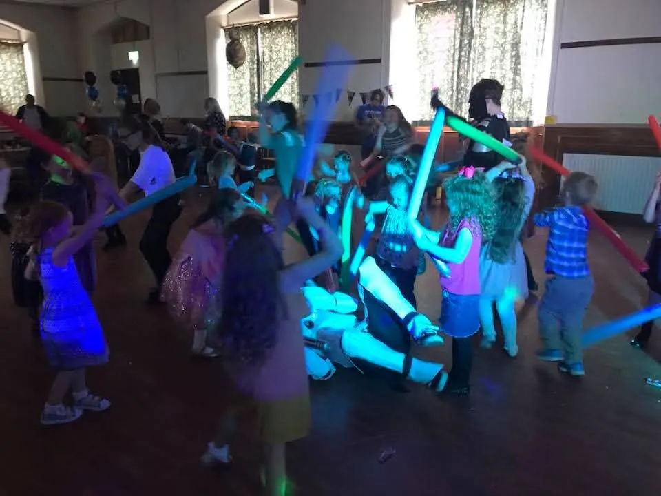 A hall of children waving glowing foam sticks under blue disco lighting